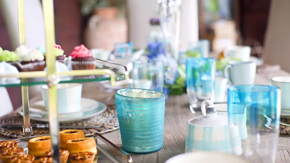 A table with a variety of desserts, glasses, and plates, set for a meal or gathering.